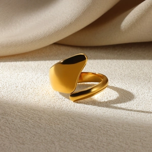 Close-up of polished gold asymmetric water drop ring on warm textured background