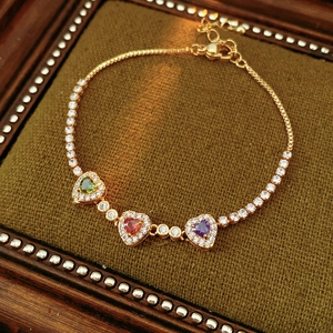 Close-up of 18k gold plated tennis bracelet with emerald, ruby, and amethyst heart stones