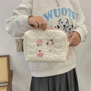 Close-up of cream quilted cosmetic bag with heart texture and cute cartoon embroidery
