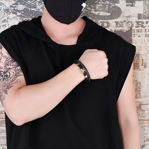 Street style shot of a man wearing a multi-layer black leather bracelet with gold cross