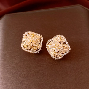 Macro shot of gold square stud earrings with clear sparkling geometric crystals on brown base