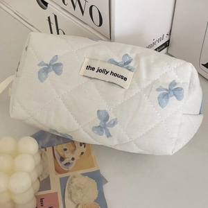 Close-up of quilted cosmetic bag featuring blue bow patterns and woven brand label