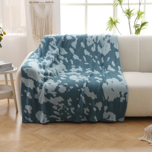 Thick knitted blanket with blue and white abstract cloud pattern on a white sofa