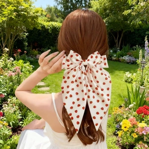 Detail of a large cream bow hair clip with strawberry prints worn in a sunny garden