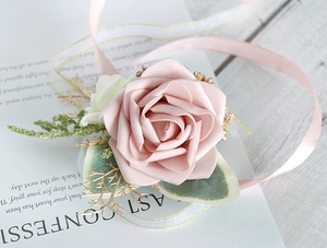 Detail of dusty pink artificial rose wrist corsage with silk ribbon and gold accents