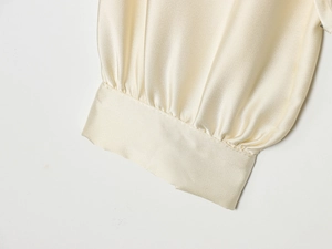 Gros plan sur la chemise en satin crème montrant les poignets plissés et la texture soyeuse