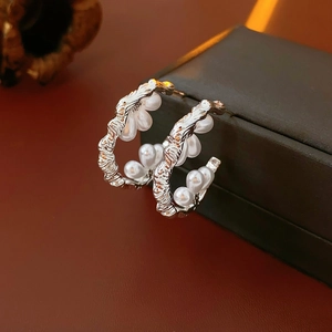 Macro detail of silver C-shaped pearl earrings with irregular textured metal on a box