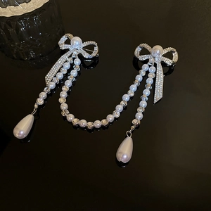 Detail of silver bow brooch with rhinestone inlay and pearl tassel on black background