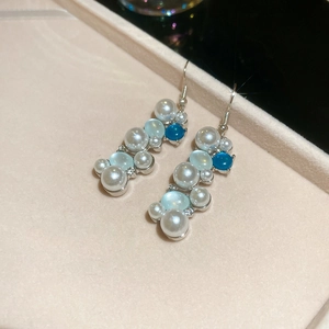 Macro shot of silver pearl and blue bead flower earrings on a beige display tray
