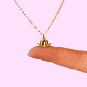 Macro close-up showing the size of the 18k gold cowboy hat pendant on a fingertip