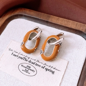 Détail macro de boucles d'oreilles émail orange avec charmes floraux argentés gravés
