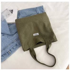 Detail of olive green canvas tote bag with fashion tag styled with denim jacket and book