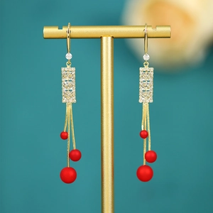 Detail of long gold tassel earrings with rhinestones and elegant frosted red beads
