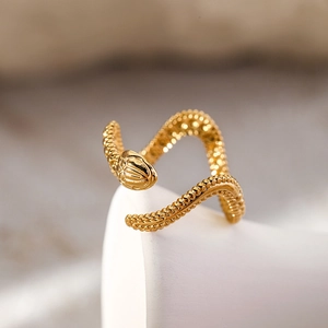 Minimalist gold snake wrap open ring featuring detailed scales on a white pedestal
