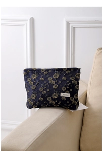 Close-up of dark blue velvet pouch with golden daisy embroidery on beige sofa armrest