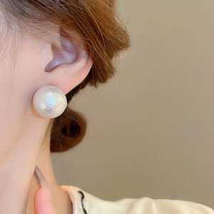 Primo piano di un grande orecchino a perla bianca con riflessi cangianti su una modella