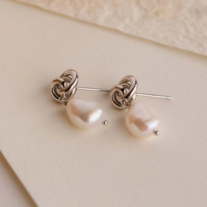 Silver twisted metal earrings with hanging irregular white pearls on textured background