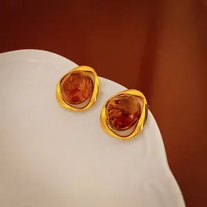 Irregular resin stud earrings in amber and gold plating on a white ceramic plate