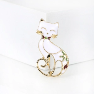 Detailed view of white enamel cat brooch with gold trim and green floral accents