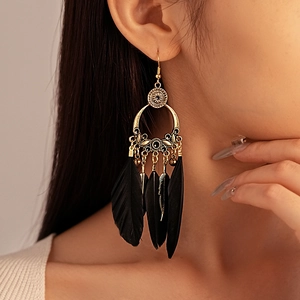 Close-up of bohemian style earrings with black feathers and gold metal tassels on model