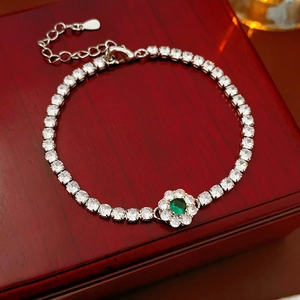 Detail of silver tennis bracelet with green flower charm on a red jewelry box