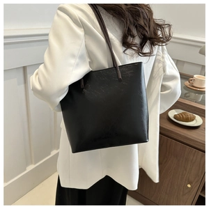 Polished black faux leather tote bag carried by model in minimalist urban setting