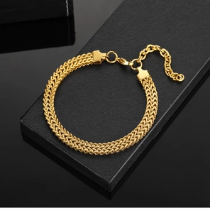 Gros plan d'un bracelet gourmette punk doré tressé posé sur un coffret cadeau noir