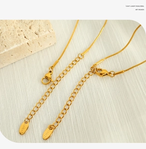 Macro detail of golden lobster clasp and s.steel engraved tag on the necklace extension