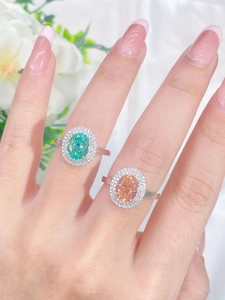 Close-up of S925 silver rings featuring oval green and orange-pink gemstones with diamond halo