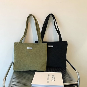 Detail view of corduroy tote bags in army green and black on a minimalist metal stool