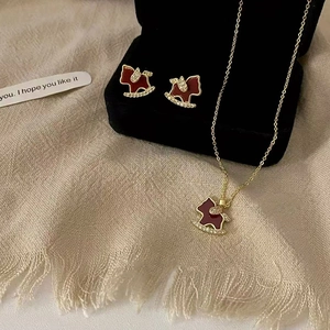 Detail view of 18K gold plated rocking horse necklace and earrings set with red enamel