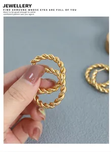 Close-up of twisted gold hoop earrings with rope texture held against a blue reflection