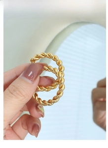 Close-up of twisted gold hoop earrings with rope texture held against a blue reflection