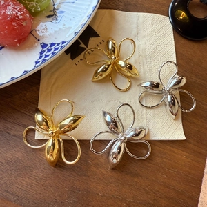 Detailed view of large gold and silver flower stud earrings on a coffee napkin