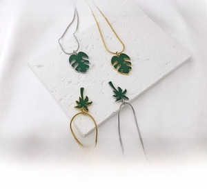 Détail de pendentifs monstera et palmier en émail vert sur acier inoxydable doré et argent