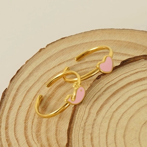Gold plated open bracelet with pink heart and dolphin charms on a wooden display