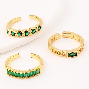 Macro detail of three-piece gold ring set featuring emerald green stones and heart design