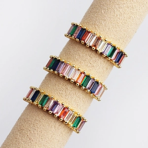 Three gold bands set with multi-color rectangular cut zircons on a beige jewelry display