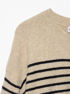 Gros plan sur la texture d'épaule du pull en maille et rayures noires sur fond beige