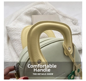 Détail d'un sac rond vert clair en cuir grainé avec une poignée jaune robuste