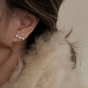 Close-up of triple pearl stud earrings on model with cozy winter clothing context
