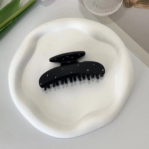 Detailed shot of a black acetate hair claw clip with colorful rhinestones in a tray