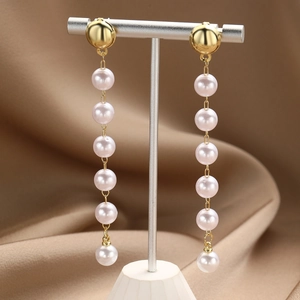 Macro detail of long gold-plated drop earrings featuring six pinkish-white pearls on a stand