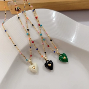 Detail of three colorful enamel heart pendants on beaded gold chains in a ceramic tray