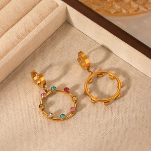Boucles d'oreilles créoles dorées 18K avec cristaux colorés sur fond beige chic
