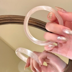 Dettaglio ravvicinato di un bracciale rigido in vetro rosa perlato con effetto occhio di gatto