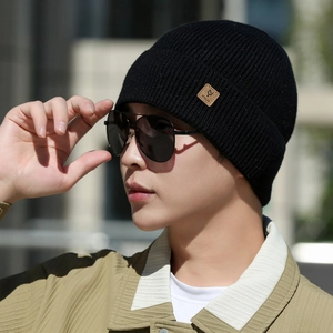 Detailed view of black ribbed knit beanie with leather patch on a male model outdoors