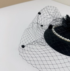 Detail of vintage black mesh veil headpiece featuring elegant pearls and soft feathers