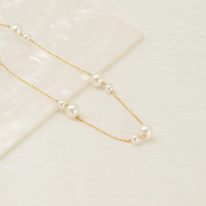 Elegant gold titanium steel necklace featuring alternating white pearls on a textured tray