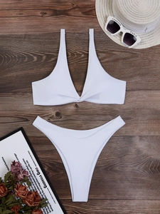 Bikini bianco allacciato al collo con cappello di paglia e occhiali su sfondo in legno